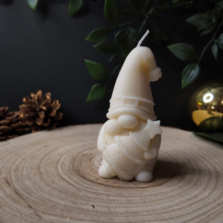 Eine weiße Kerze in Form eines Gnoms mit einem Hut, umgeben von Tannenzweigen und einer Weihnachtskugel.